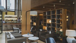 A modern lounge area with leather sofas, round tables, and a bar with a variety of bottles. - Hotel Zenit San Sebastián (San Sebastián)