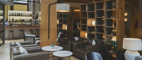A modern lounge area with leather sofas, round tables, and a bar with a variety of bottles.