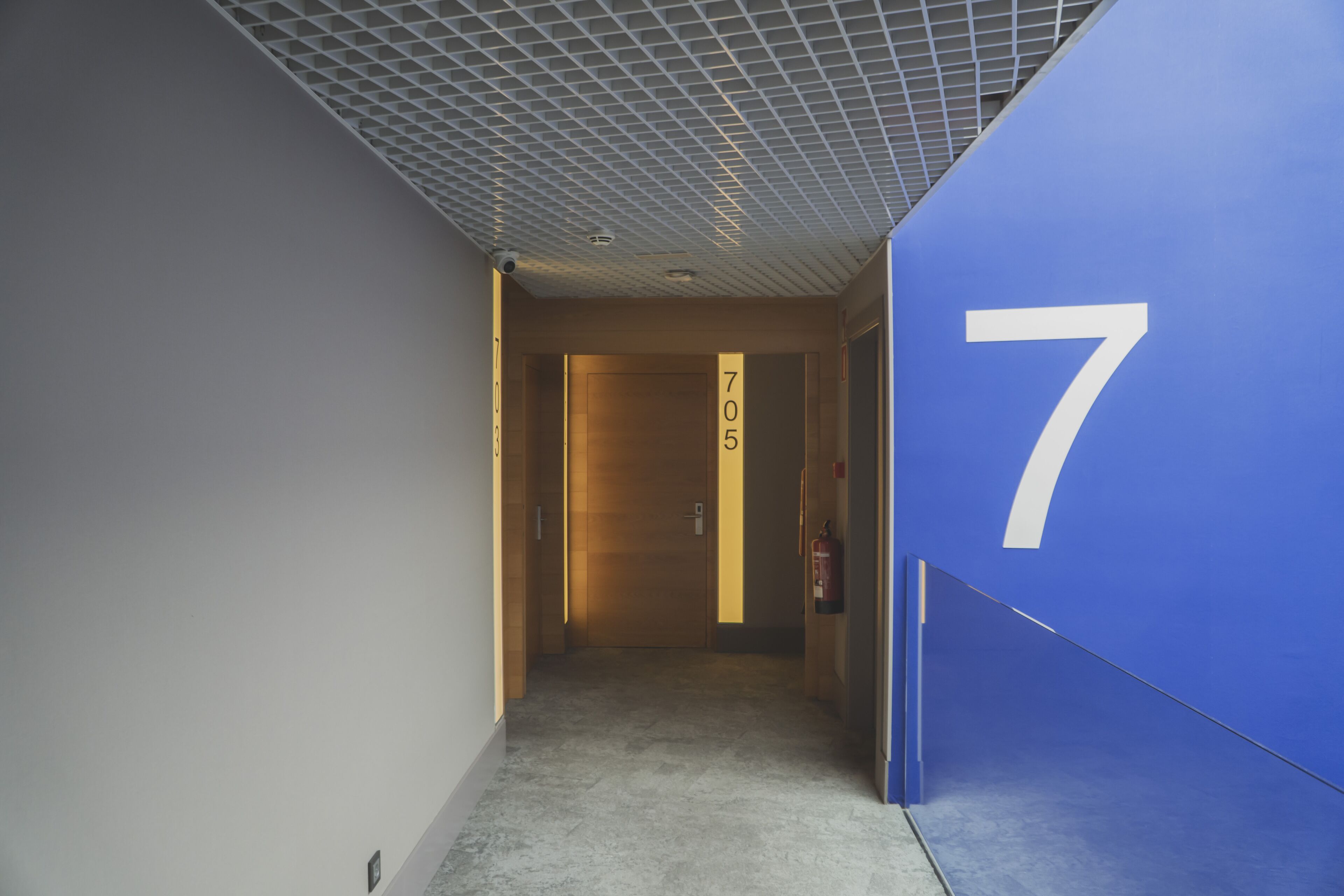 A hallway with a blue wall on the right, a number '7' sign, and a door labeled '705'.