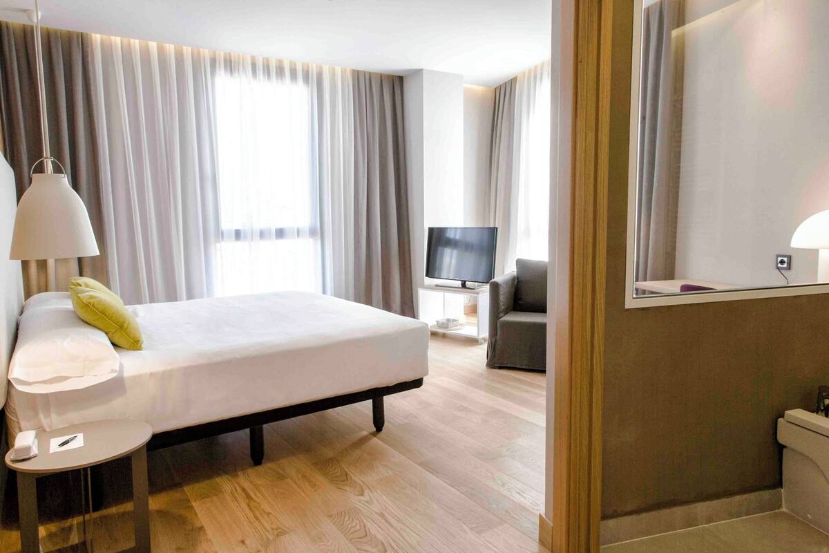 A hotel room with a bed, bedside table, lamp, TV, and a bathroom.