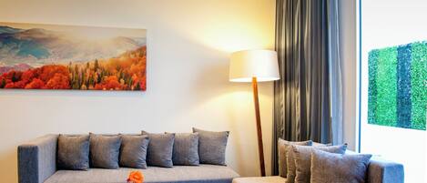 A modern hotel room with a grey sofa, a round wooden coffee table, and a painting of autumn foliage on the wall.