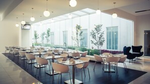 A modern dining area with tables and chairs, large windows, and hanging lights. - Fiesta Inn Plaza Central Aeropuerto (Mexico City)