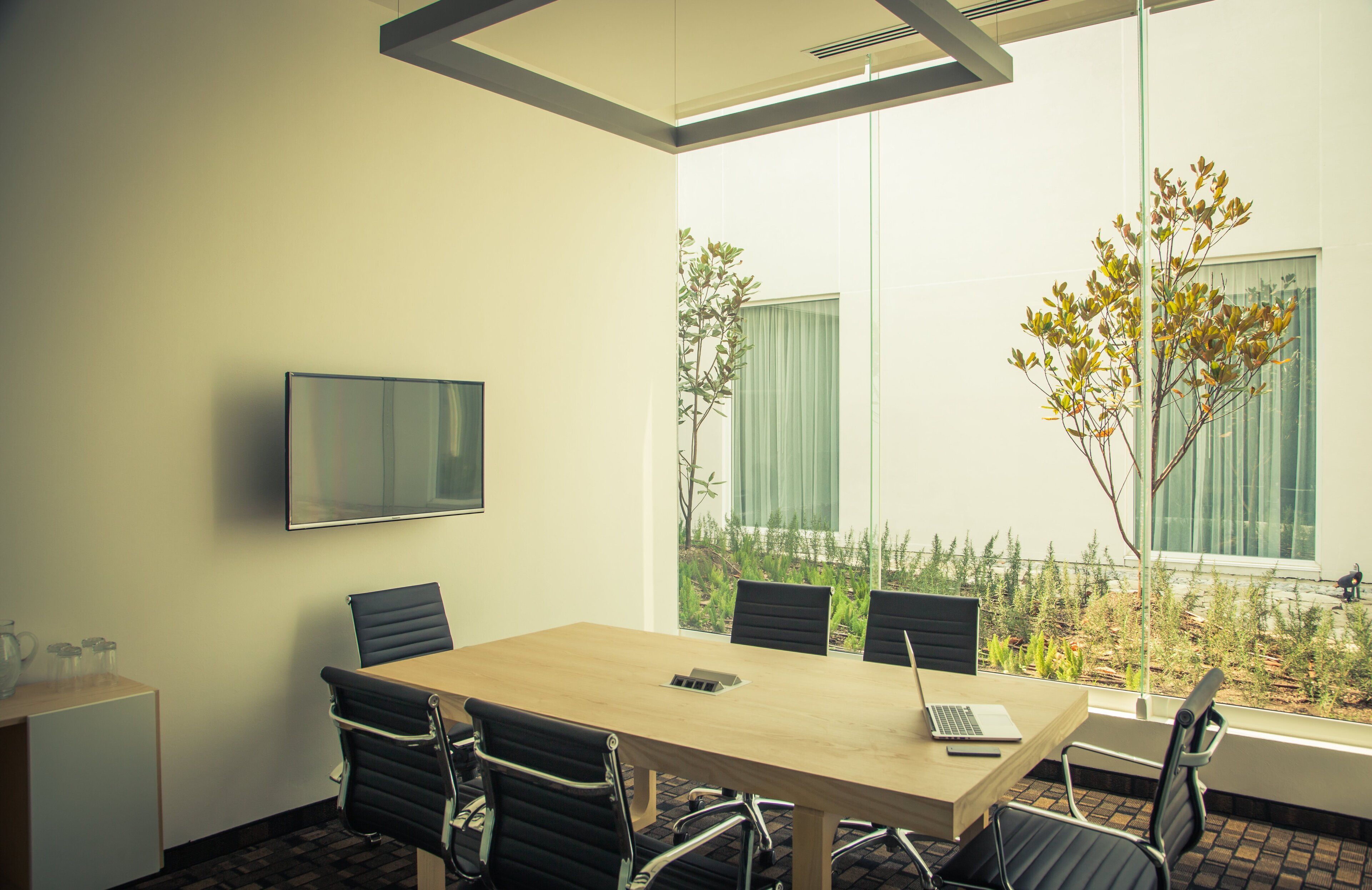 A conference room with a wooden table, black chairs, a laptop, and a TV on the wall.