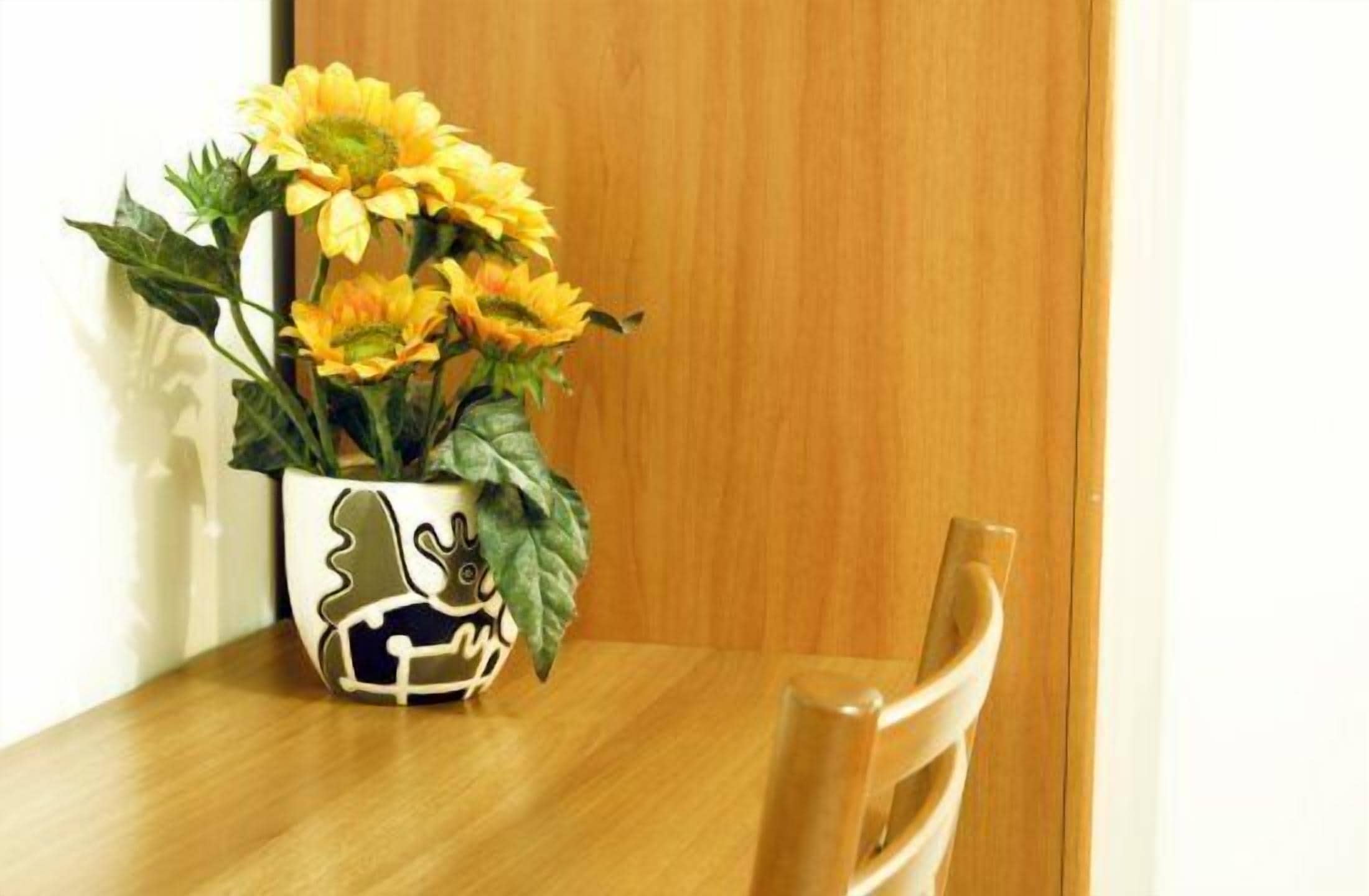 Une table en bois sur laquelle est posé un vase blanc contenant des fleurs jaunes.