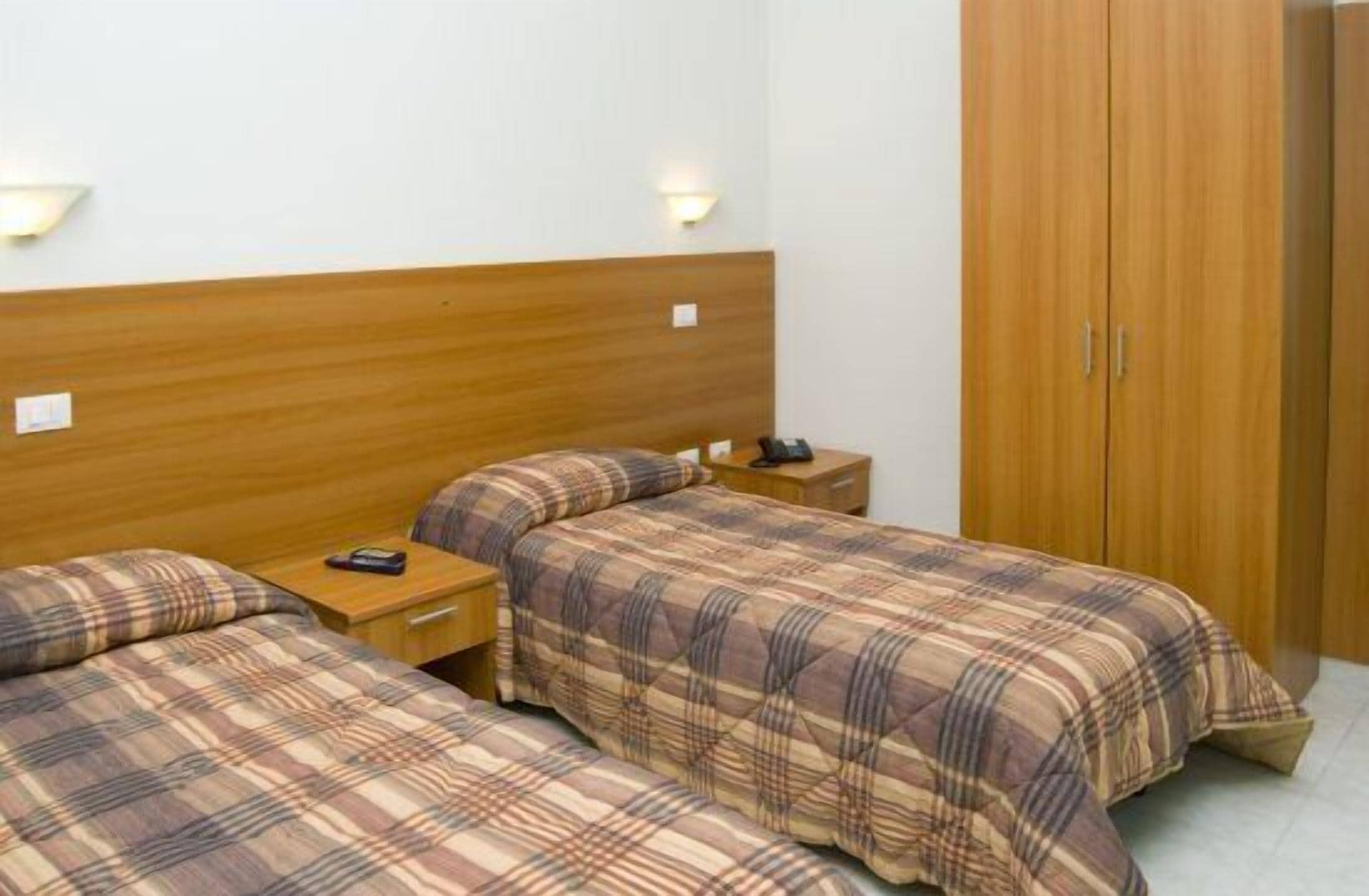 Camera d'albergo con due letti, una testiera in legno, comodini e un armadio.