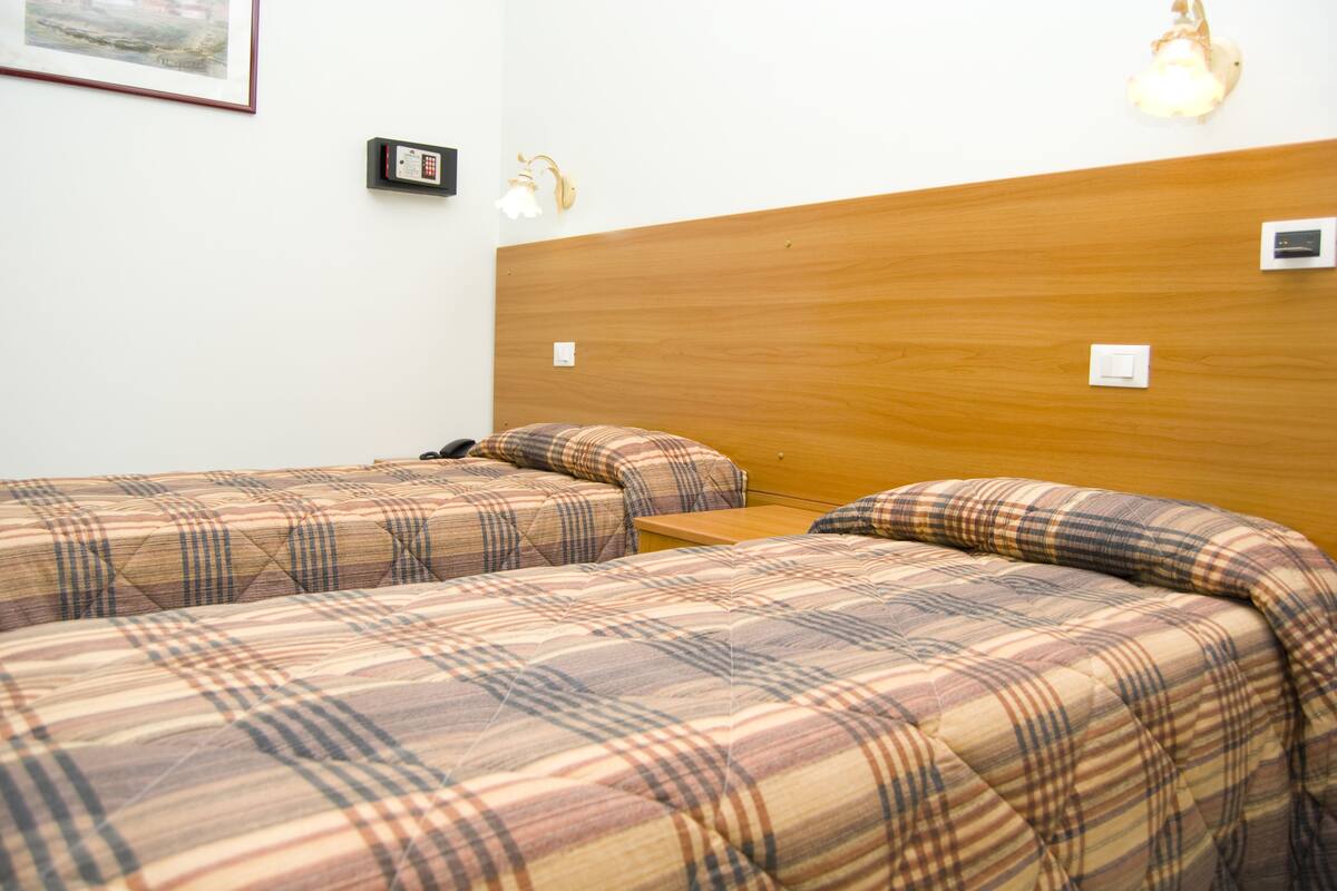 Une chambre avec deux lits, chacun doté d’une couette à motifs écossais, d’une tête de lit en bois et d’un luminaire fixé au mur.