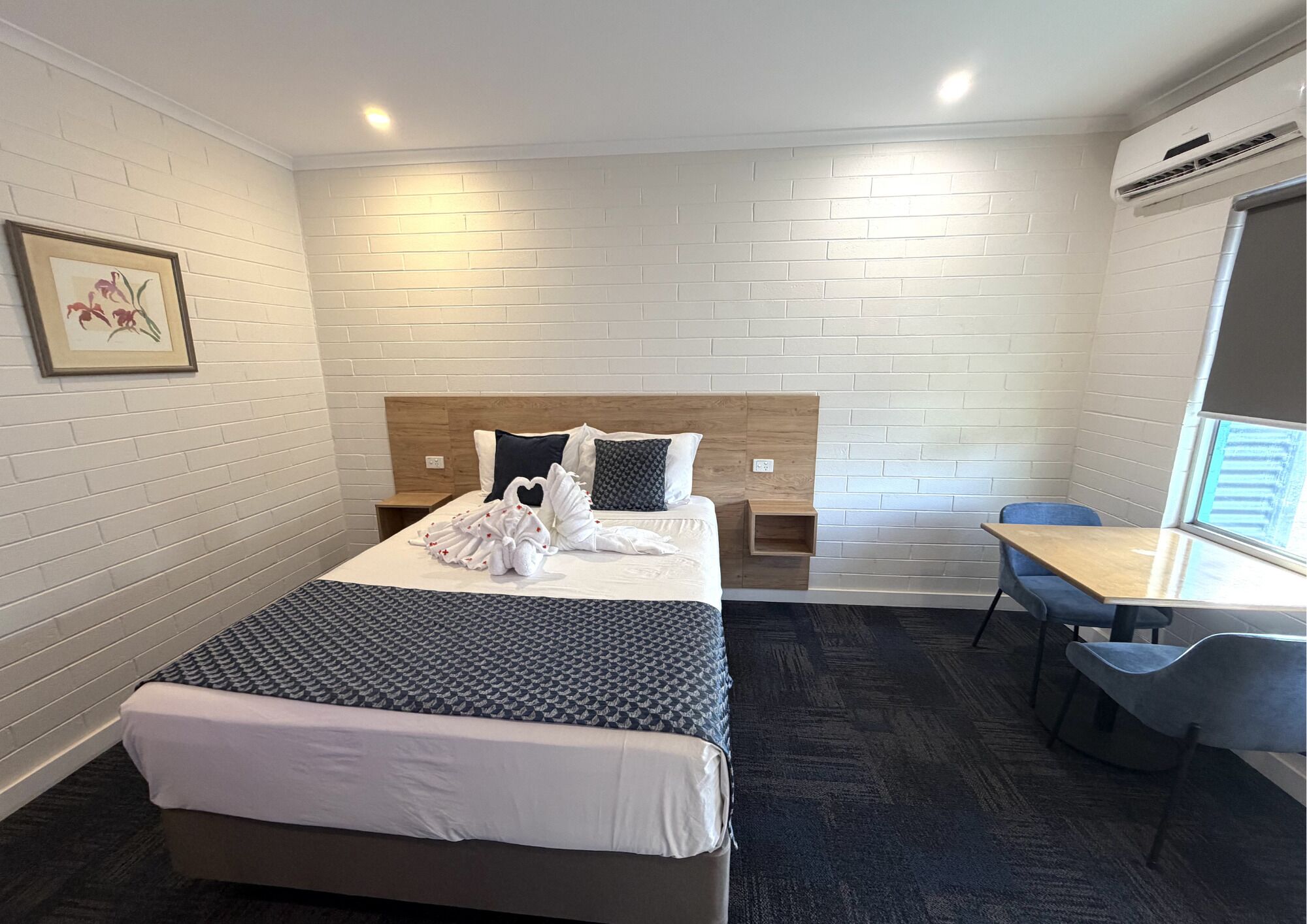 Una habitación de hotel con cama, mesita de noche, silla y un pequeño escritorio con otra silla.