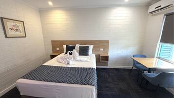 Una habitación de hotel con cama, mesita de noche, silla y un pequeño escritorio con otra silla.