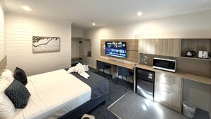Une chambre d’hôtel moderne équipée d’un lit, d’un bureau, d’une télévision et d’une kitchenette.