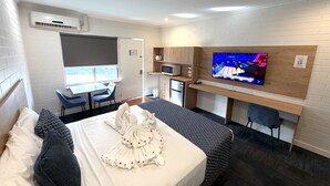 Une chambre d’hôtel comprenant un lit, un bureau avec un ordinateur, une télévision et une petite kitchenette.