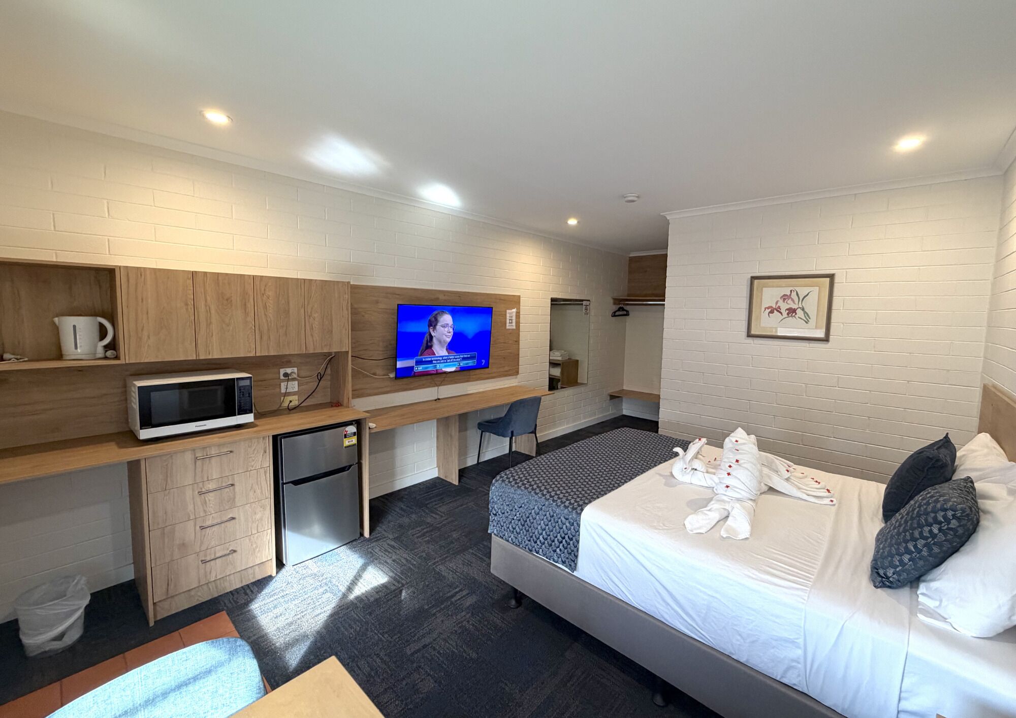 A hotel room with a bed, a desk with a TV, a microwave, a mini-fridge, and a small kitchenette.