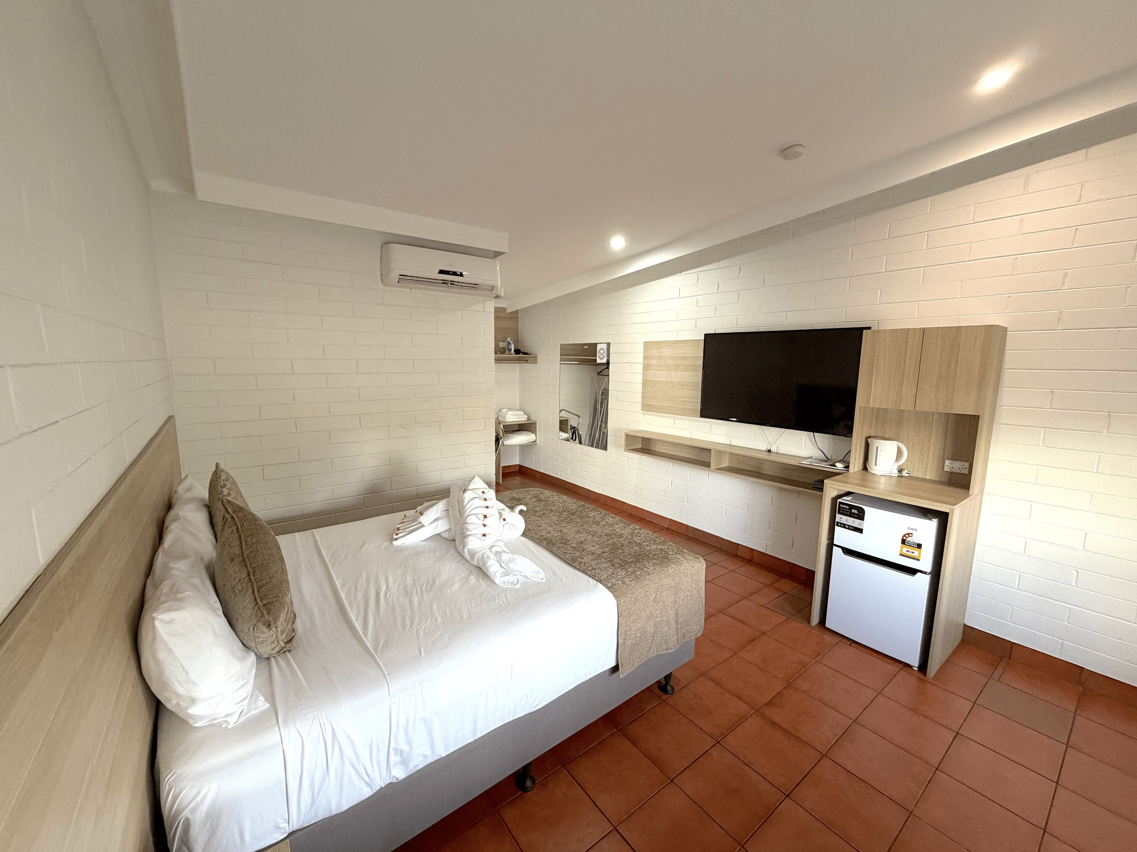 A hotel room with a bed, a TV, a small kitchenette, and a bathroom.