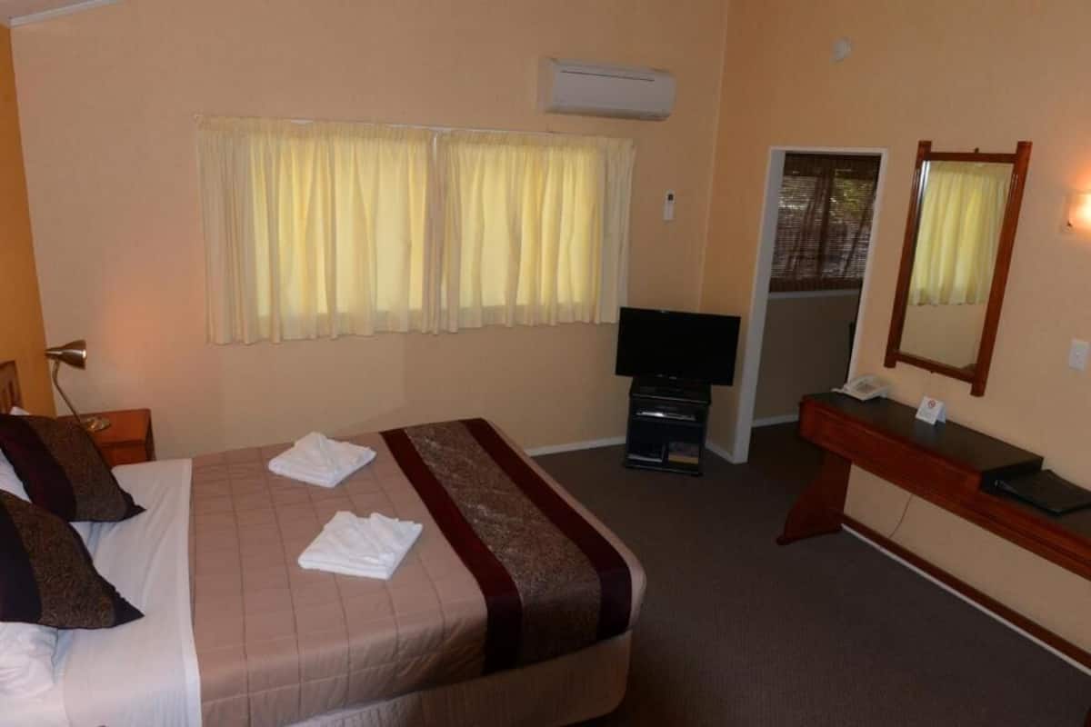 A hotel room with a bed, a desk, a television, and an air conditioning unit.