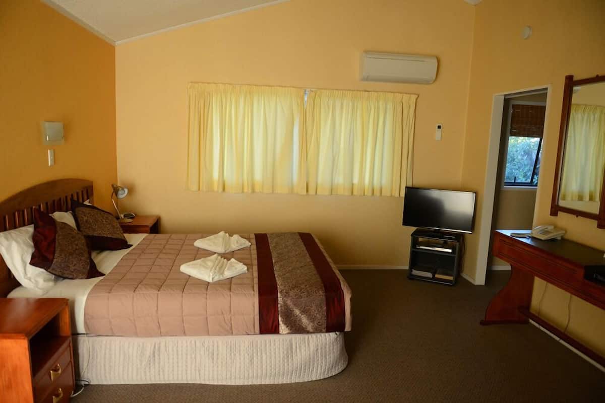 A hotel room with a bed, a TV, a desk, and a window with curtains.