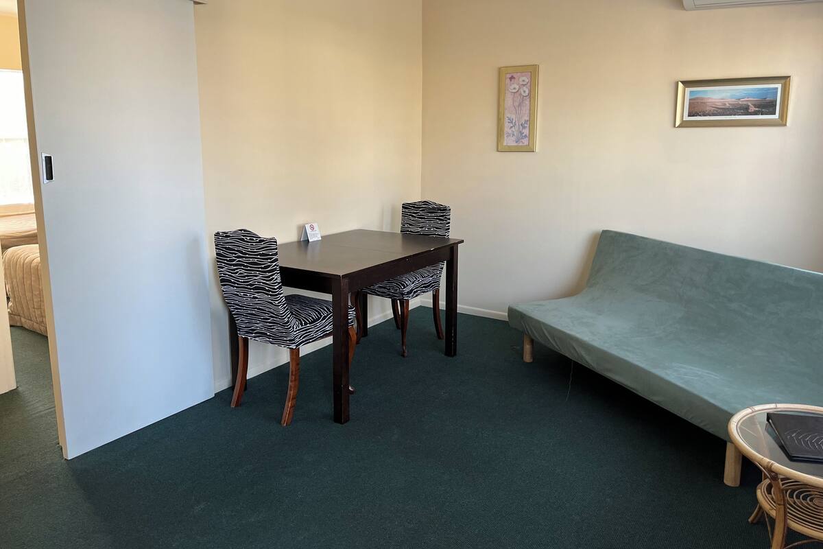 A room with a dining table, two chairs, a sofa, and a small table with a laptop.