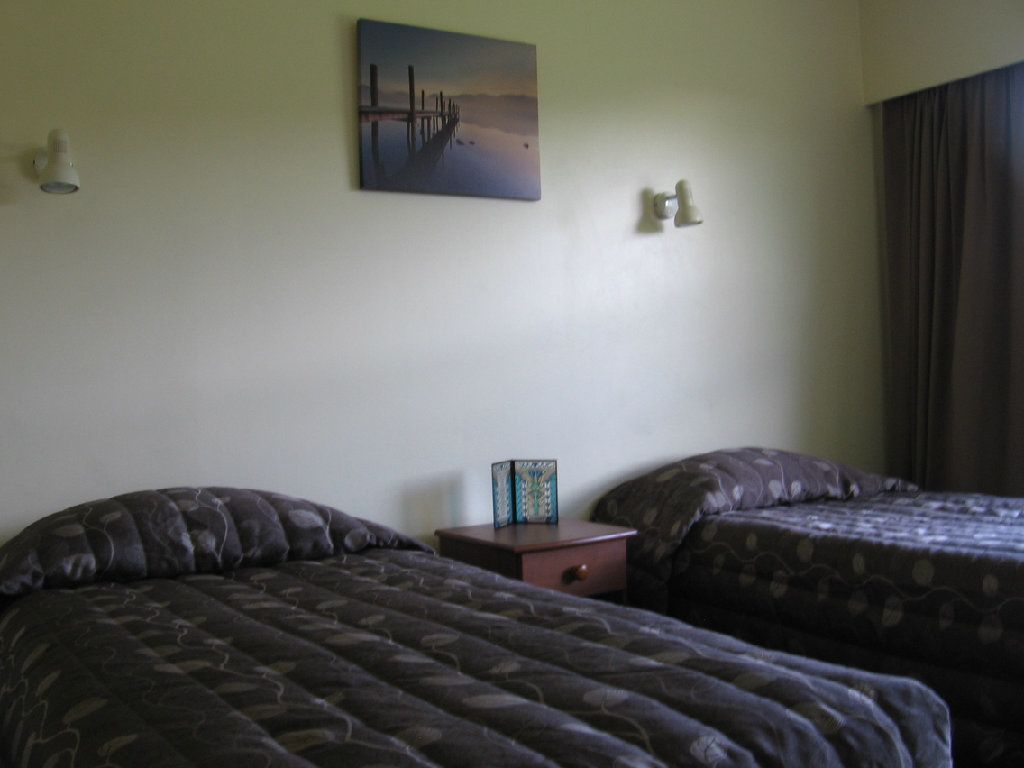 Una camera d'albergo con due letti, un comodino, un quadro e una lampada.