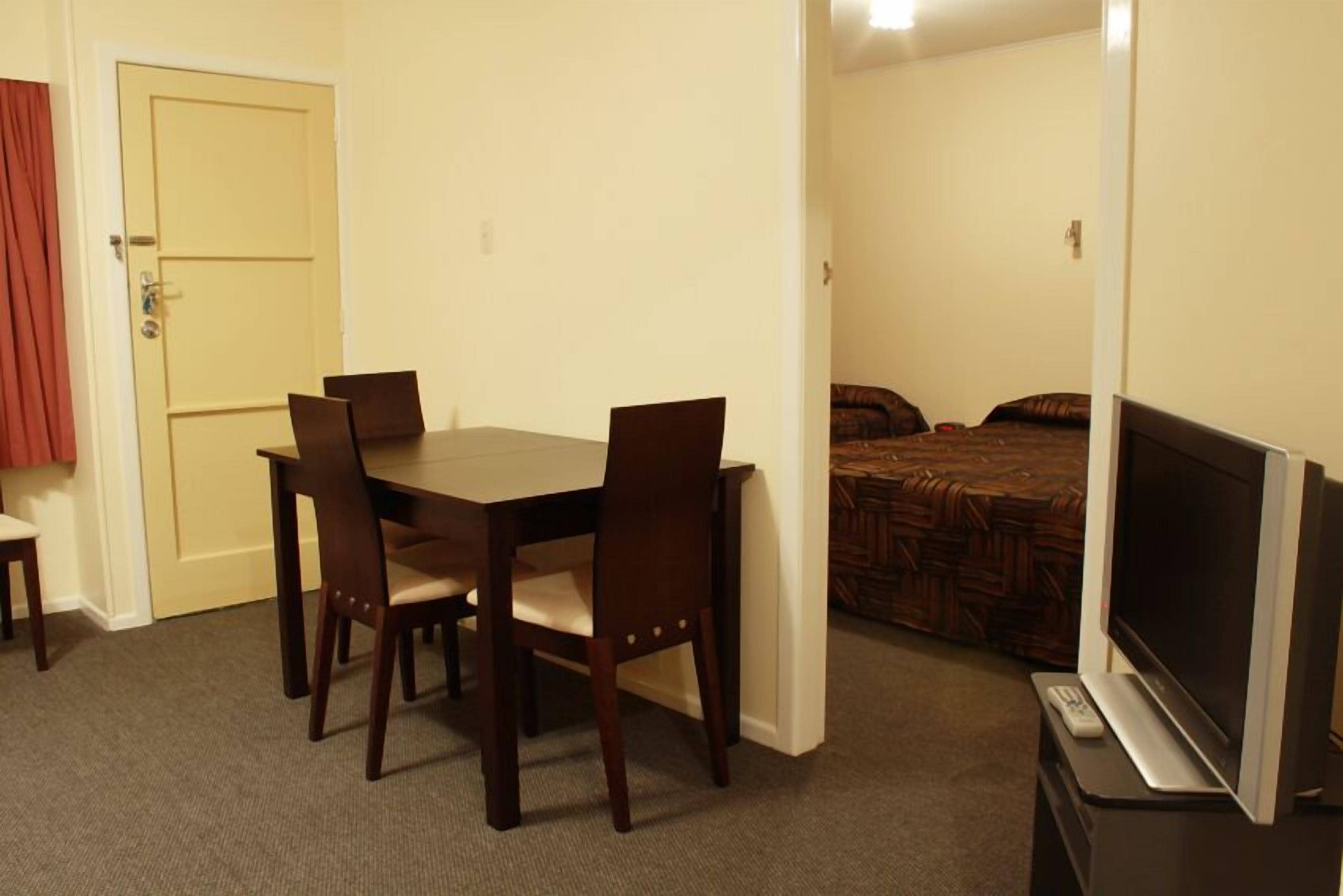 Una habitación de hotel compacta con una mesa de comedor y sillas, un televisor y una cama con una colcha estampada.