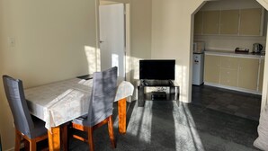 Un coin repas avec une table et des chaises, un téléviseur et, au fond, une cuisine.