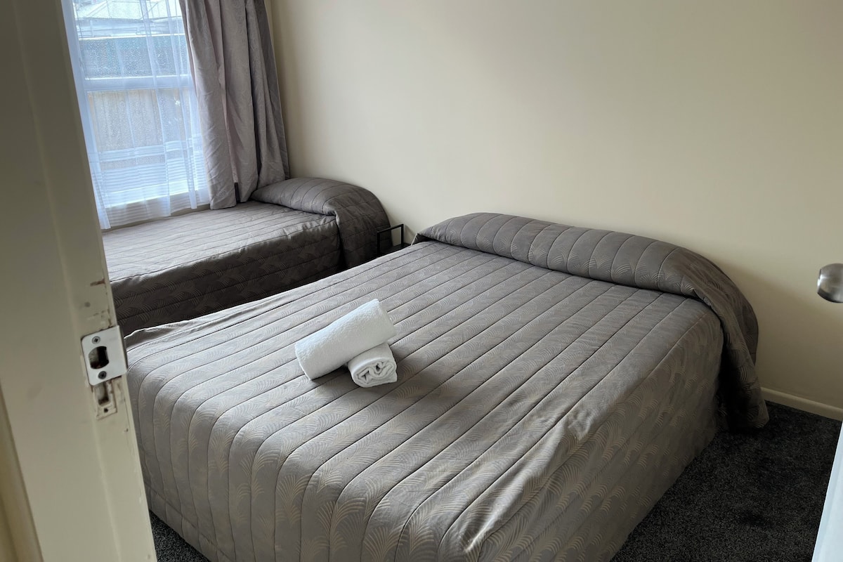 A hotel room with two beds, one with a headboard and the other without.