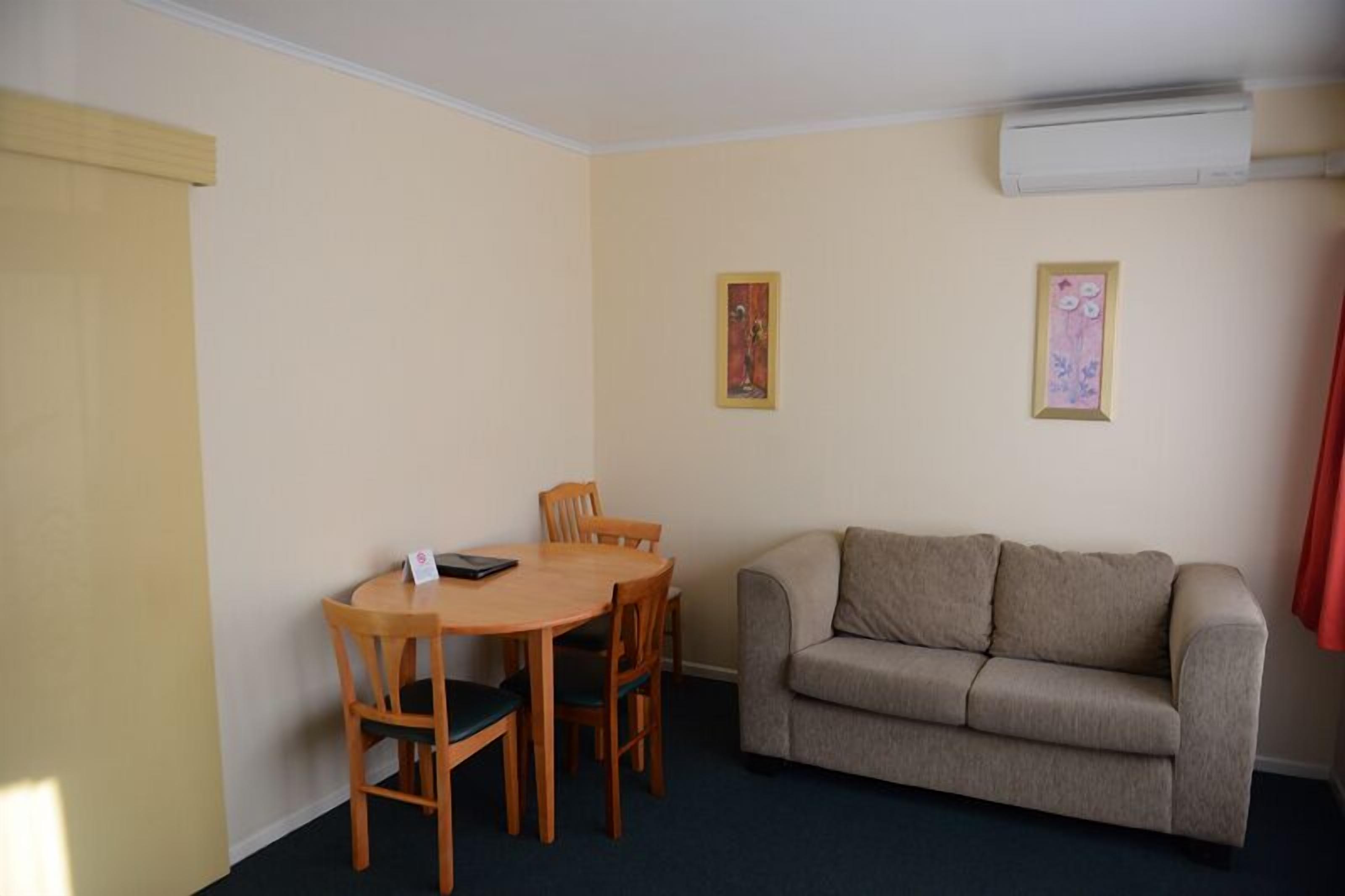 Una sala pequeña con un sofá beige, una mesa de comedor de madera con sillas y dos cuadros en la pared.