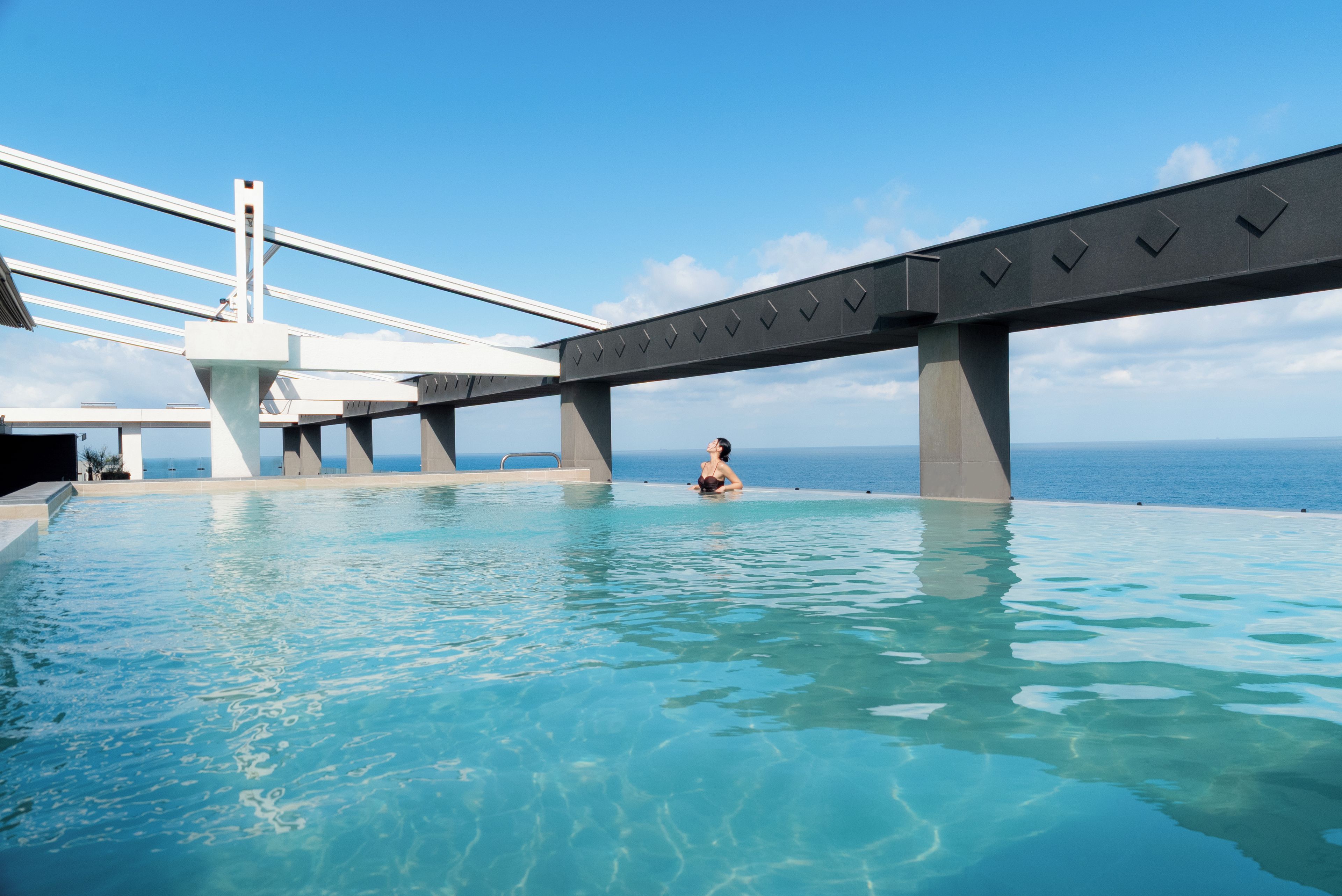 Ein Pool mit einer Person im Wasser, einer Brücke und einem wolkenlosen Himmel.