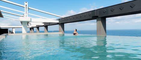Une piscine avec une personne assise dans l’eau, un pont et un ciel dégagé.