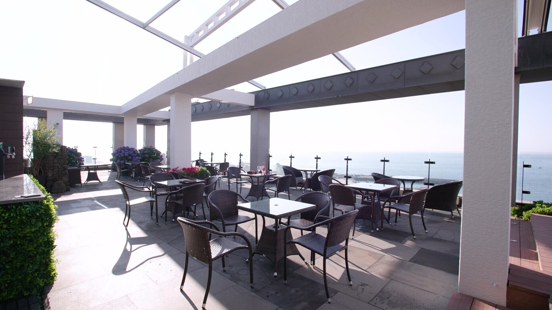 Een terras buiten met tafels en stoelen, met uitzicht op de zee.