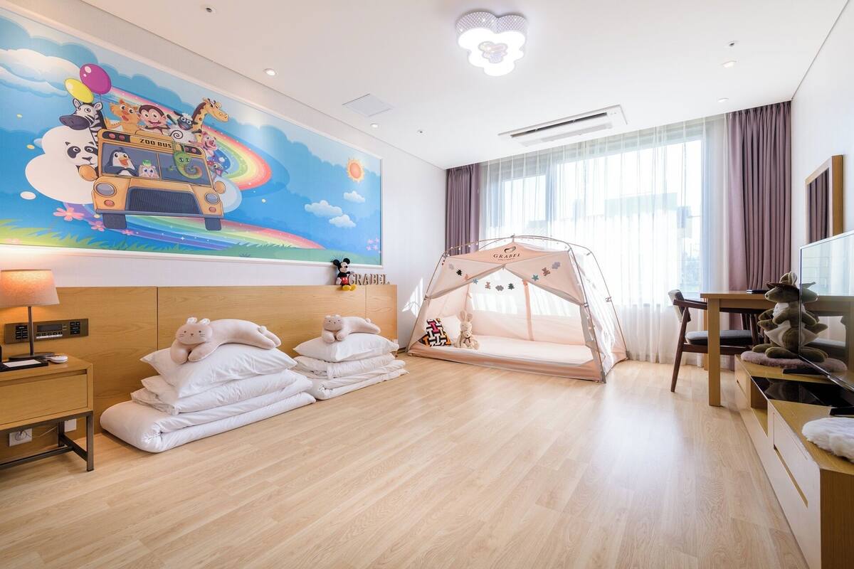 Hotelkamer met een bed, nachtkastje, lamp, raam met gordijnen, wanddecoratie, een tentachtige constructie en een televisie.