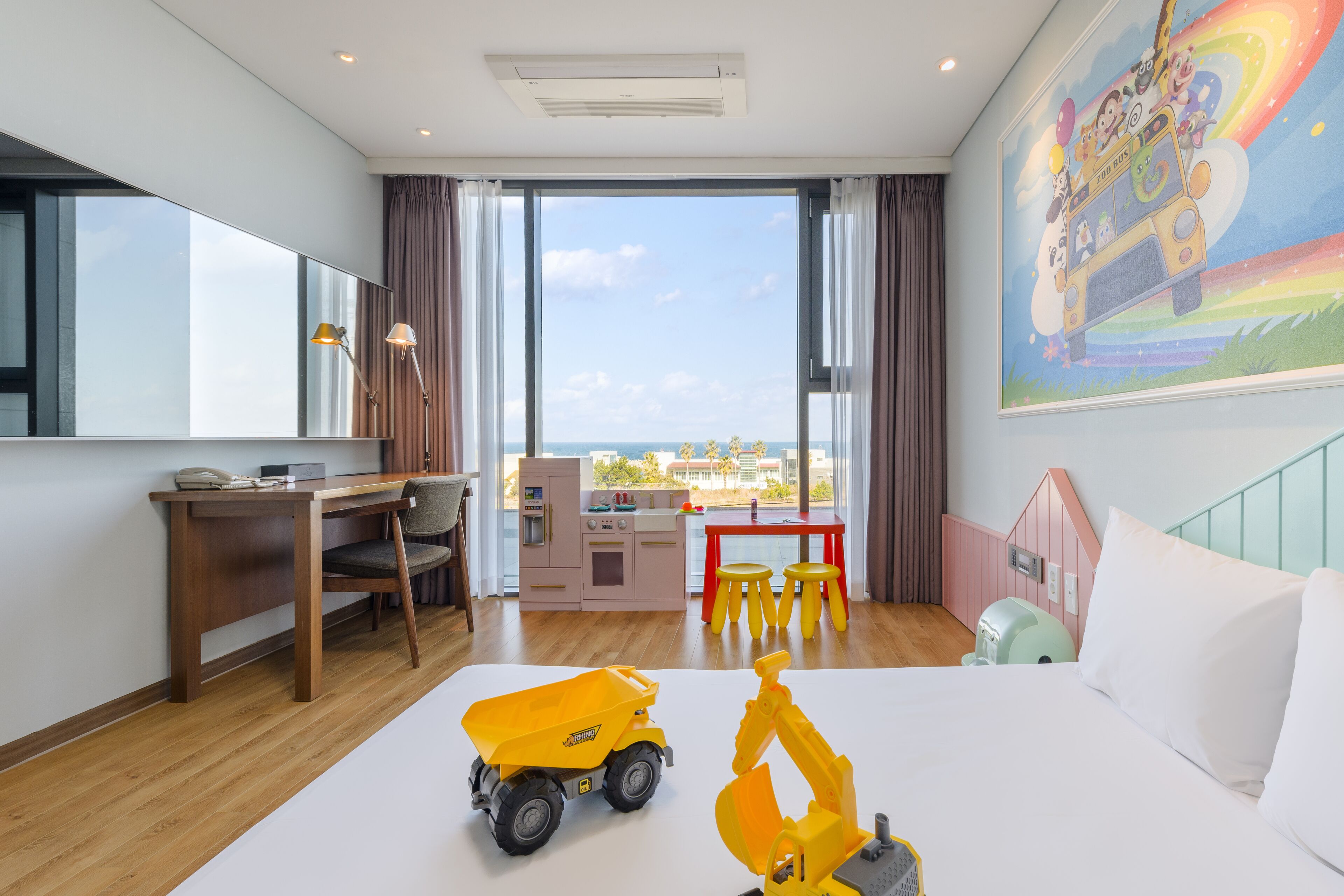 A hotel room with a large window, a desk, a bed, and children's toys.