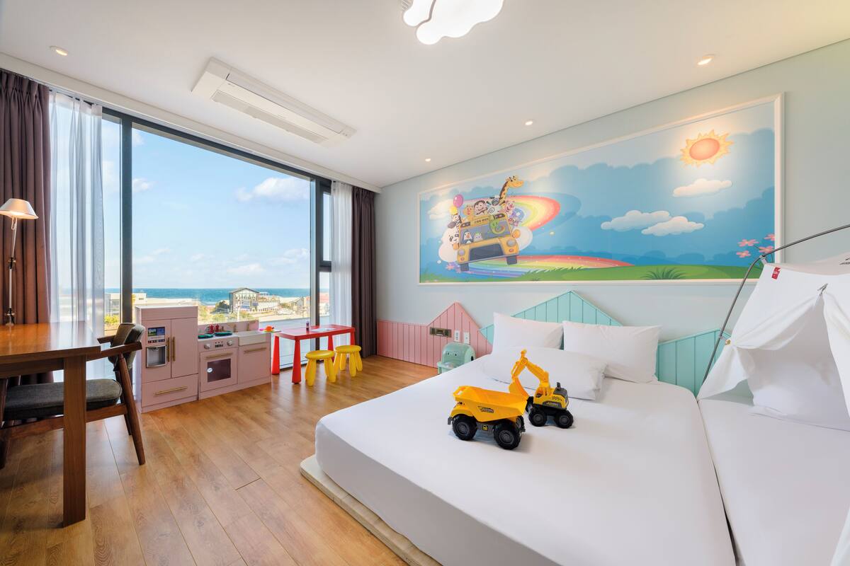 Een hotelkamer met een groot bed, een bureau met stoel, een kitchenette en uitzicht op de oceaan.