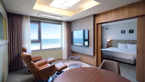 Habitación de hotel con un ventanal grande, un televisor de pantalla plana, una cama, un área de descanso con sillas y una mesa redonda.