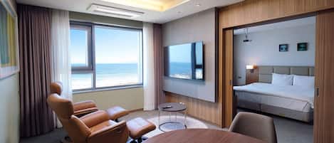 A hotel room with a large window, a flat-screen TV, a bed, a seating area with chairs, and a round table.