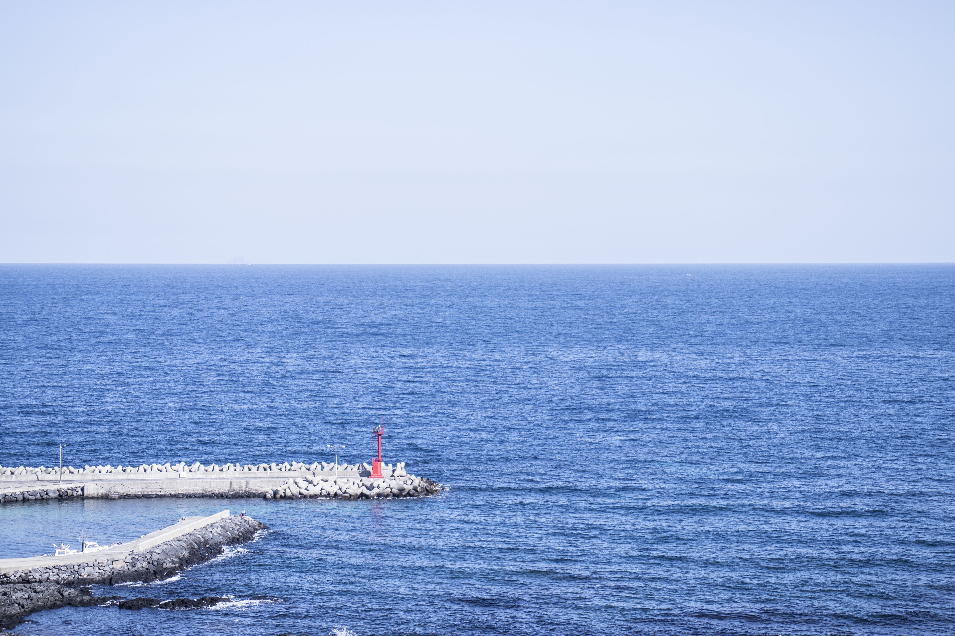 Une scène côtière avec une jetée s’avançant dans la mer, et un phare rouge en évidence.