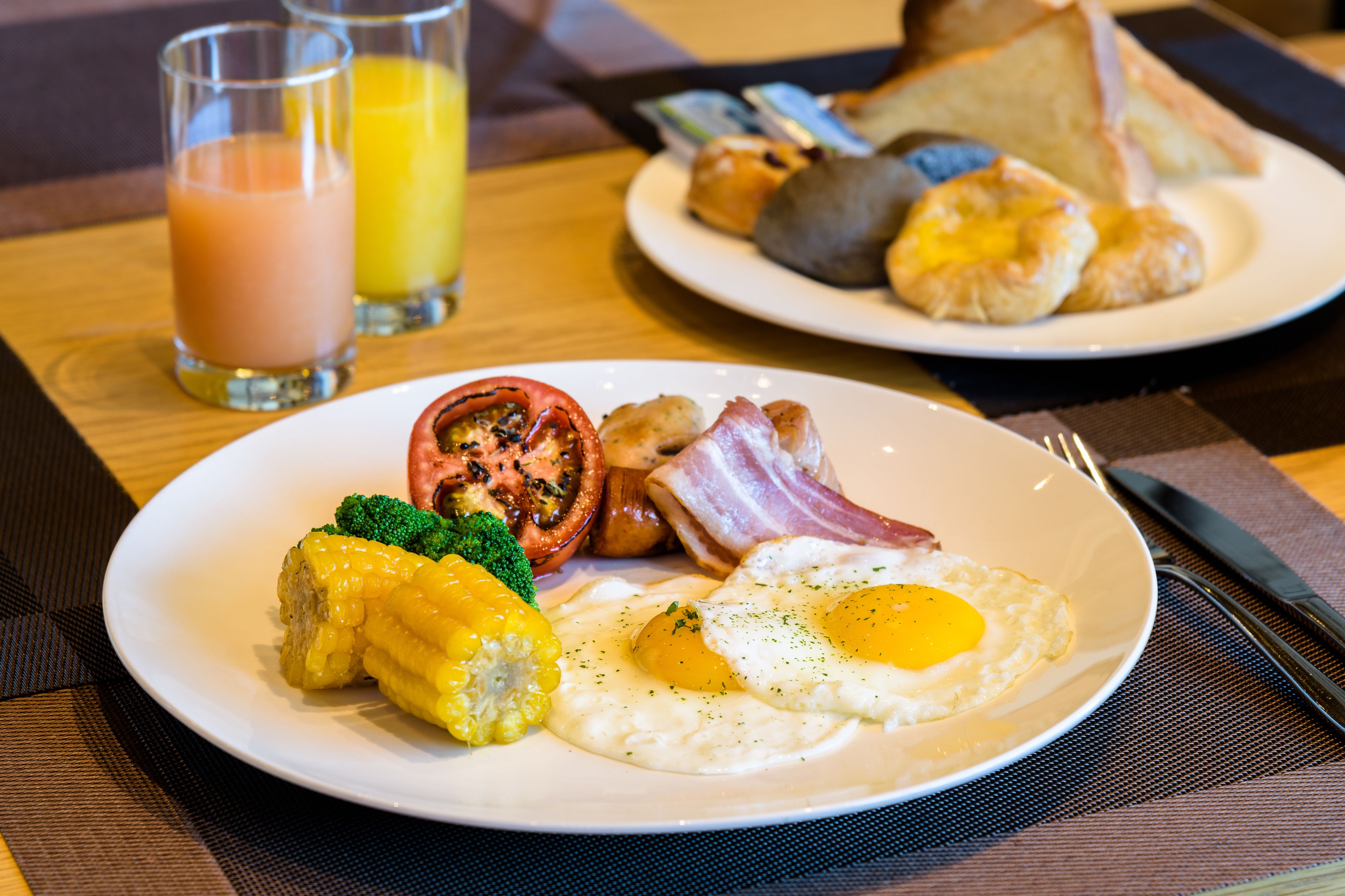 A breakfast plate with eggs, bacon, tomatoes, and corn on a white plate.
