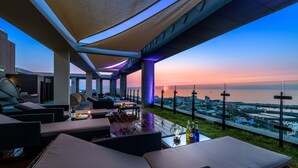 Una terraza al aire libre con asientos, vistas de la ciudad y una puesta de sol.