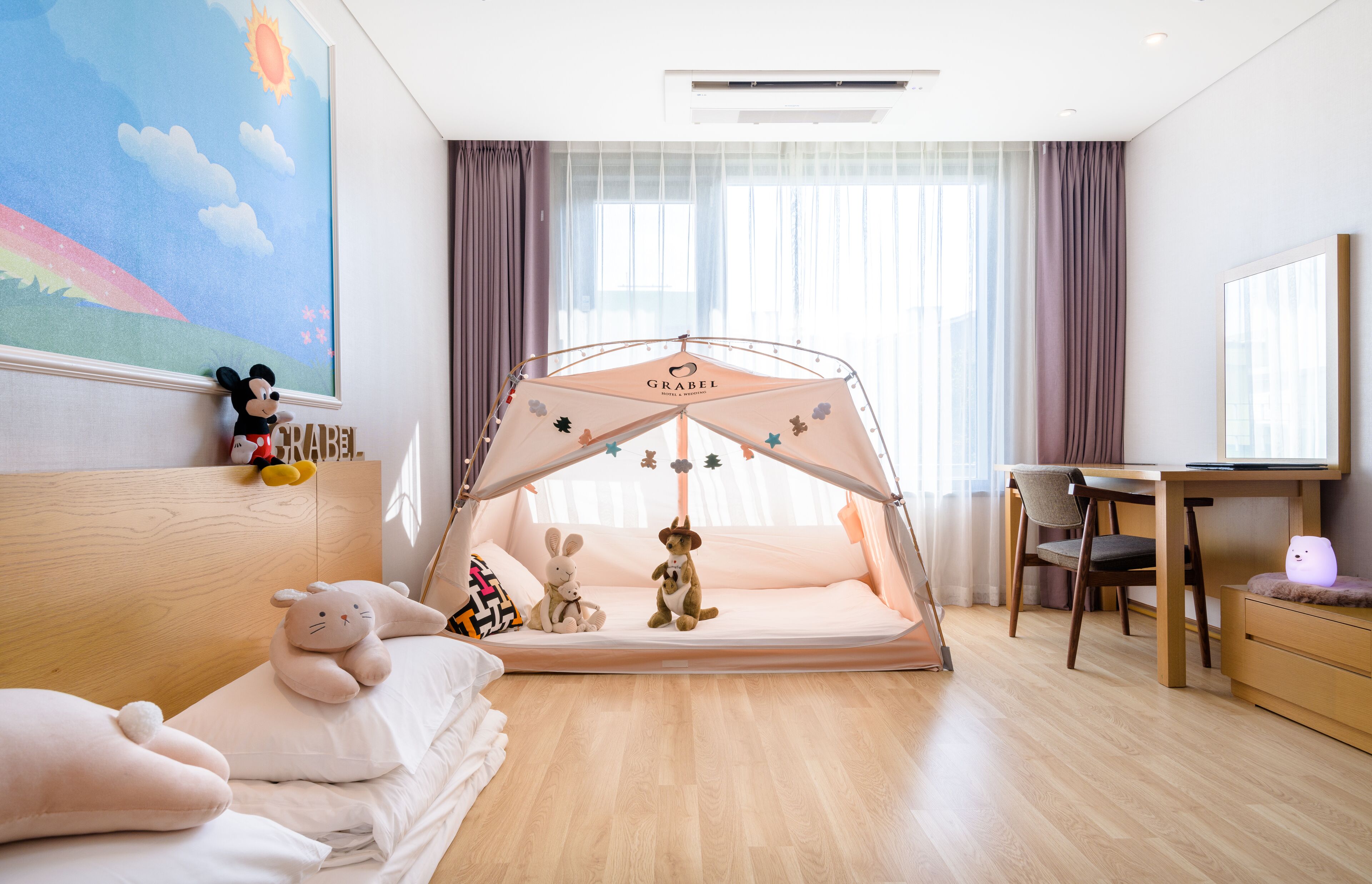 A child's room with a tent, plush toys, a bed, a desk, and a window with curtains.