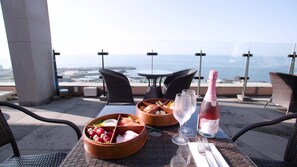 A table set with a bottle of champagne, a bowl of fruit, and bread on a terrace with a view of the sea. - Grabel Hotel Jeju (Jeju City)