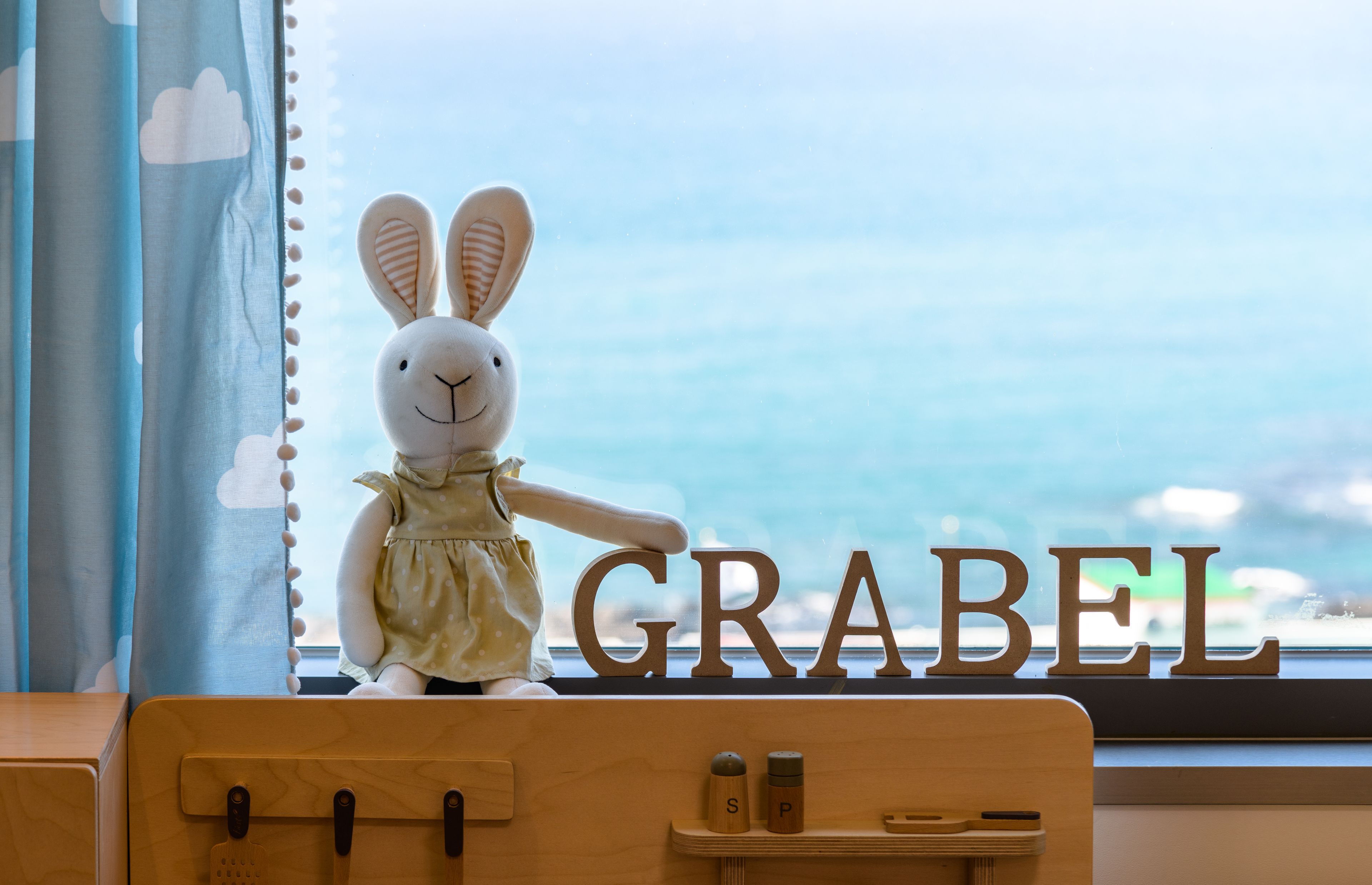A plush toy rabbit on a wooden dresser with the word "GRABEL" in the background.