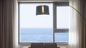Una habitación con un ventanal grande que ofrece vistas al mar, una lámpara colgante negra y un sofá gris.