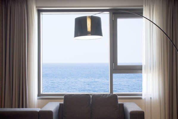 Una habitación con un ventanal grande que ofrece vistas al mar, una lámpara colgante negra y un sofá gris.