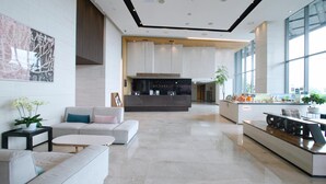 Un vestíbulo amplio con una mesa de recepción, zona de estar y ventanas grandes.