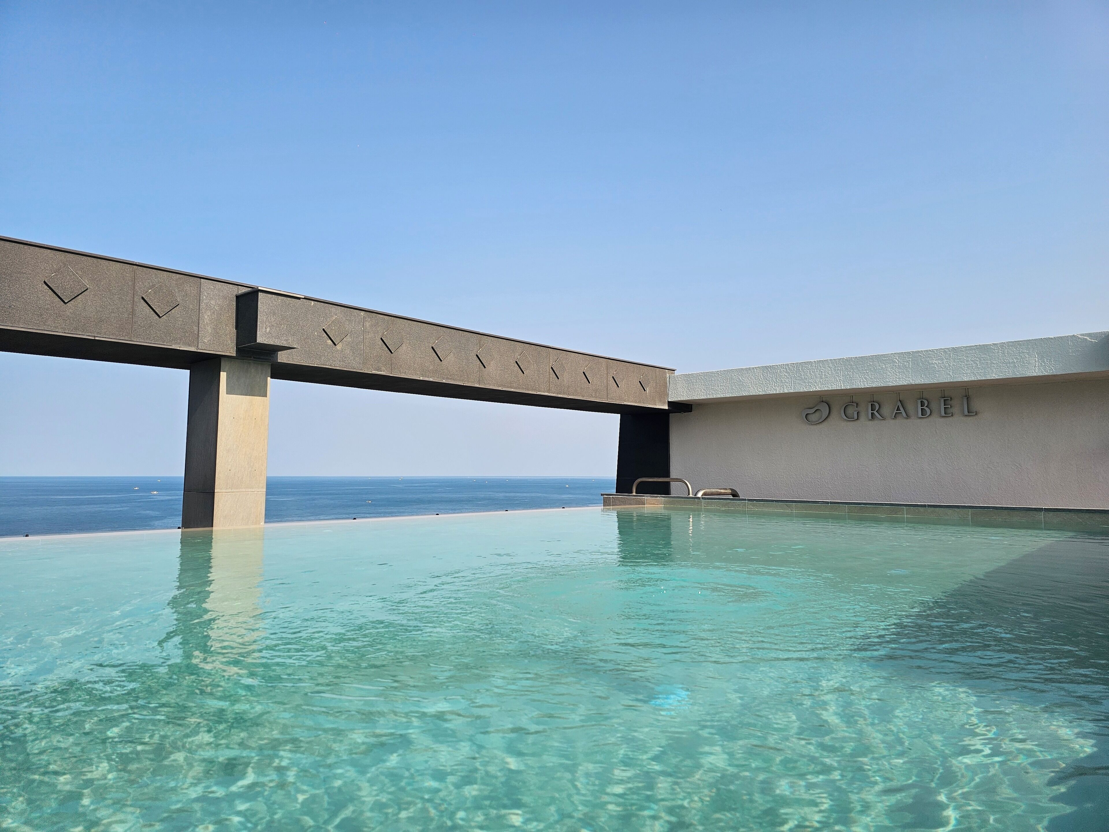 Un área de piscina con agua cristalina, una estructura de hormigón en lo alto y una pared con el nombre 'GRABEL'.