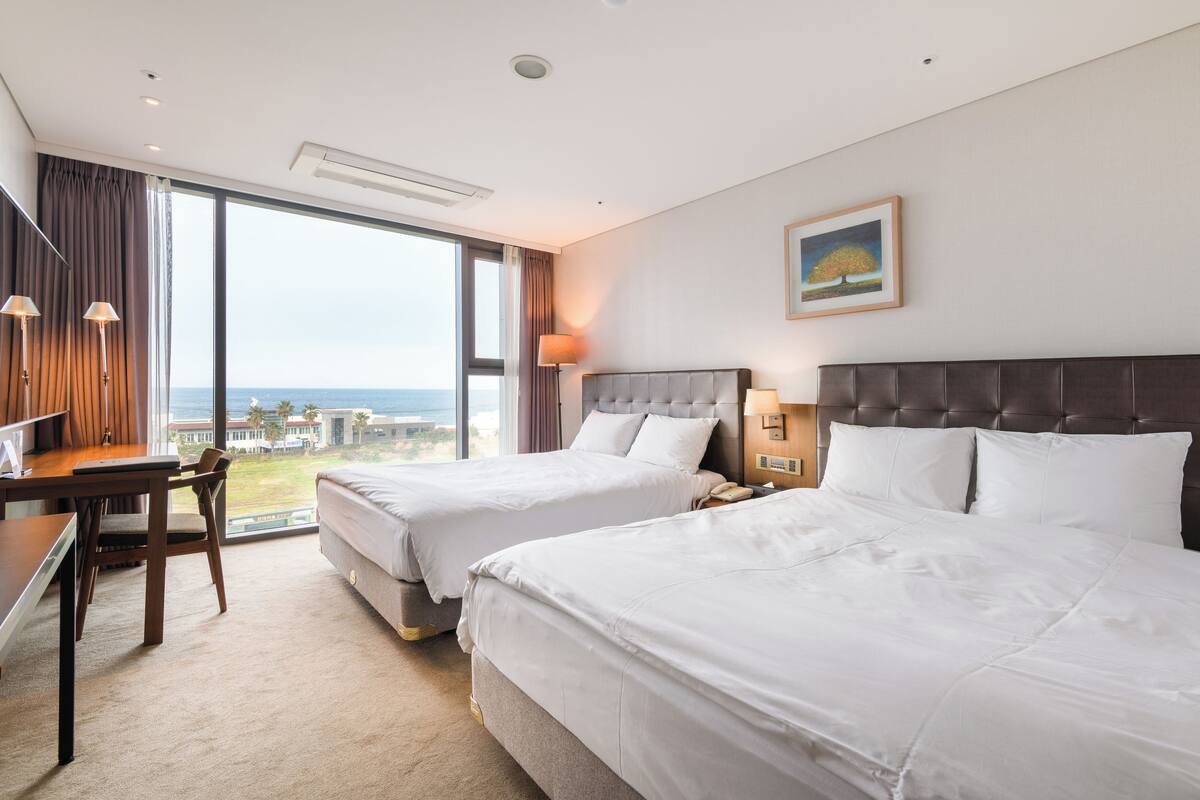 Een hotelkamer met twee bedden, een bureau en uitzicht op de oceaan.