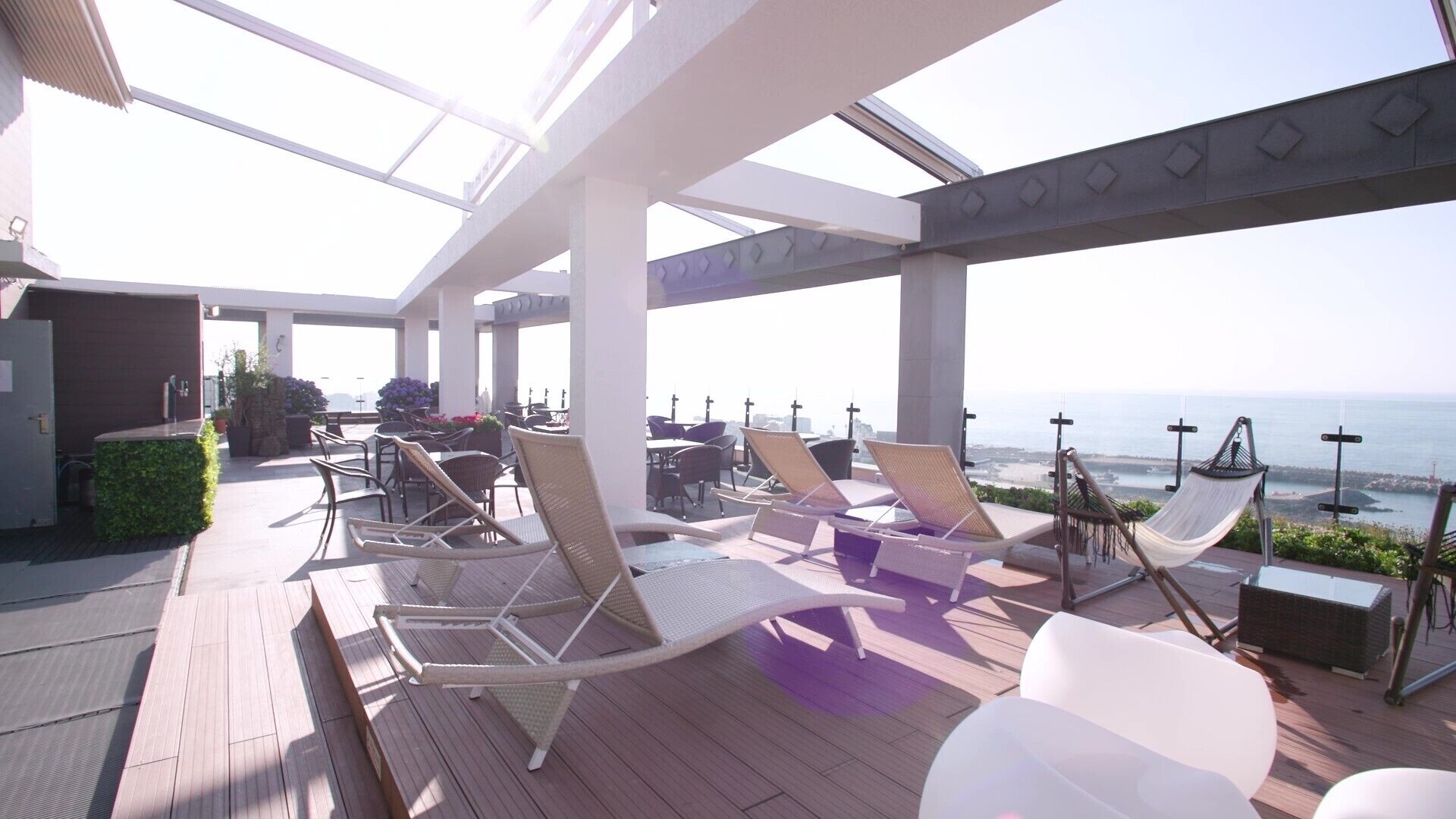 A sunlit outdoor lounge area with lounge chairs and a hammock, overlooking a coastal view.