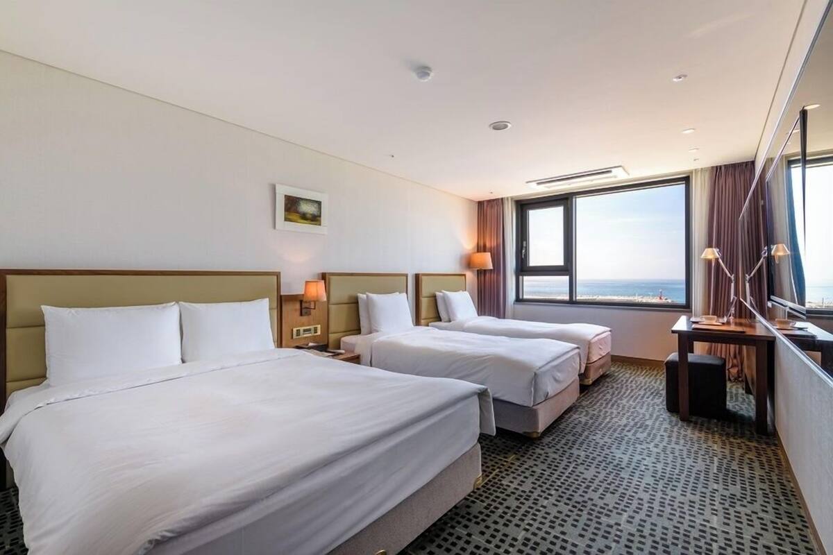 Een hotelkamer met twee bedden, een groot raam en uitzicht op zee.