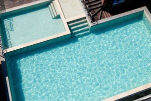 Una piscina rectangular con agua cristalina y azul, rodeada por una solería y una barandilla de metal.