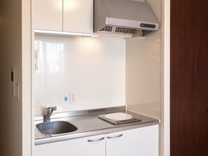 A compact kitchen with a built-in sink, a microwave, and a stove. - Hotel Hakata Place (Fukuoka)
