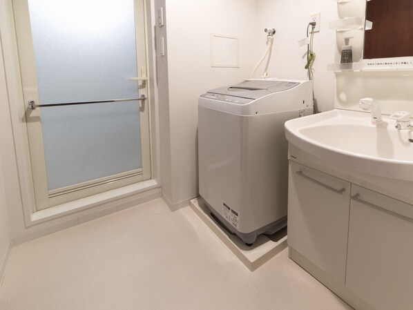 A bathroom with a white sink, a mirror, and a washing machine. - Hotel Hakata Place (Fukuoka)