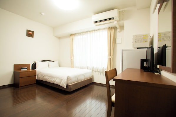 Habitación de hotel con cama, mesita de noche, escritorio, silla, aire acondicionado, ventana con cortinas y televisor de pared.