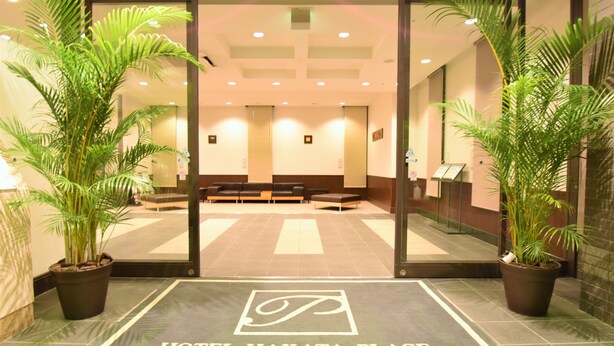 A hotel entrance with a reception area, seating, and potted plants.